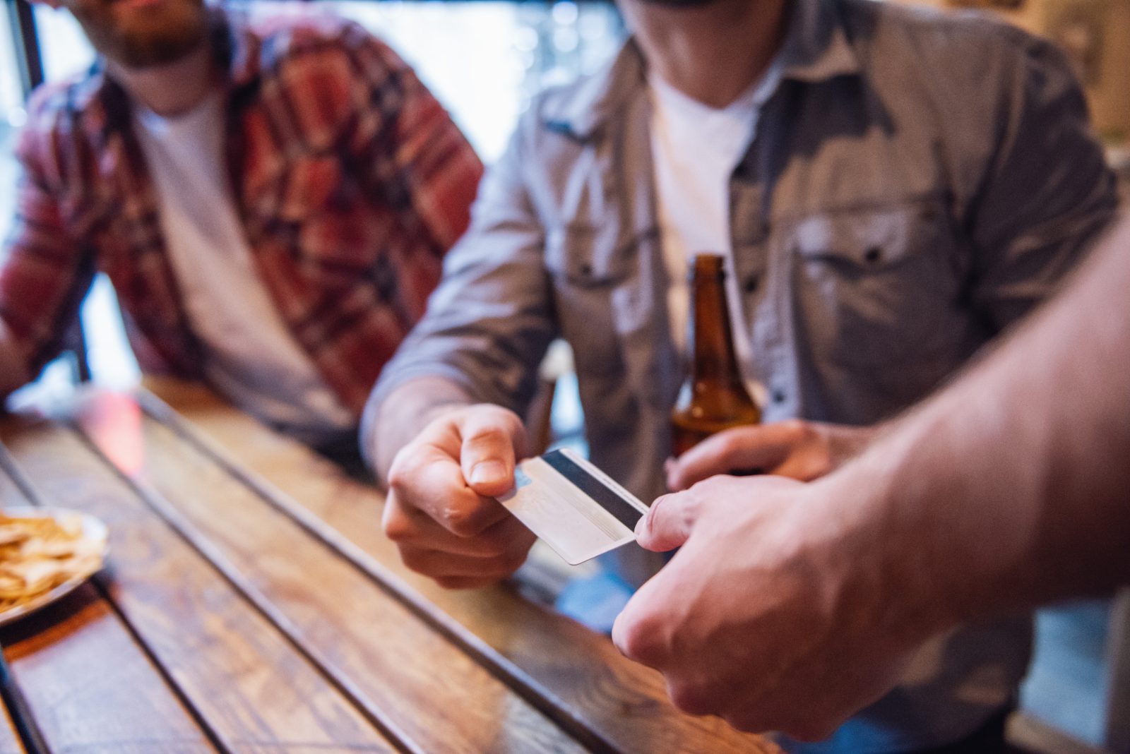 Young man handing a card across a bar table while holding a beer